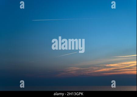 Aerei commerciali che affettano il grande cielo blu sopra Sussex con i loro contrali al tramonto, Hove, East Sussex, Inghilterra. Foto Stock