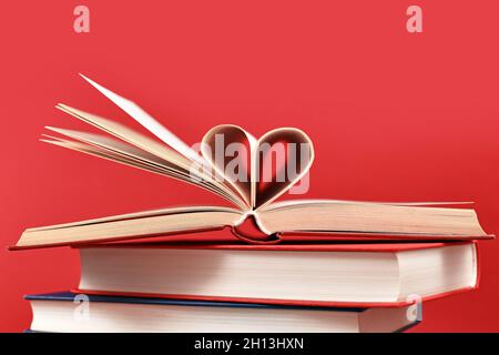 Pagine piegate a forma di cuore su una pila di vecchi libri di copertina rigida su sfondo rosso Foto Stock