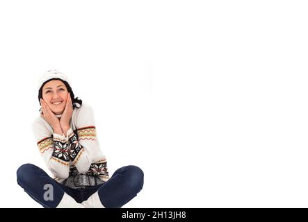 Ragazza caucasica allegra in un caldo cappello e un maglione a maglia si siede su uno sfondo bianco Foto Stock