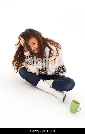 Curly allegra ragazza caucasica in un caldo maglione siede su uno sfondo bianco Foto Stock