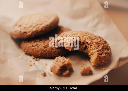 Sulla carta da imballaggio beige ci sono tre deliziosi biscotti salubri di farina d'avena, uno dei quali è morso. Torte fatte in casa. Foto Stock