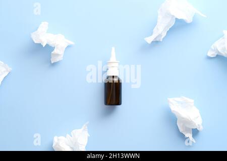 Bottiglia spray idratante nasale e fazzoletti di carta su sfondo blu pastello. Disposizione piatta, vista dall'alto. Influenza, trattamento del freddo concetto. Foto Stock