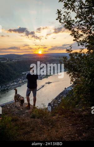 Uomo silhouette con le sue quattro zampe compagni leali guardare la valle del Reno al tramonto a Sankt Goarshausen Foto Stock