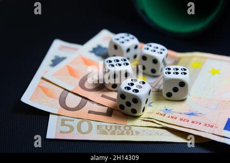 Primo piano di un tavolo in cui ci sono cinque dadi a sei lati su circa 50 euro bollette accanto a un calice con spazio copia Foto Stock