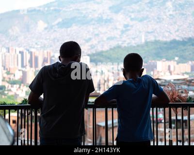Bambini che appoggiano sul ringhiere di una terrazza che contempla la vista del comune 13, un quartiere turistico a Medellin, Colombia Foto Stock