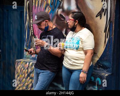 Medellin, Antioquia, Colombia - 6 gennaio 2021: Uomo latino e donna mangiare un gelato appoggiarsi contro un muro Foto Stock