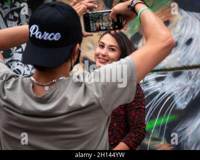 Medellin, Antioquia, Colombia - 6 gennaio 2021: L'uomo latino con un cappuccio nero che dice 'Parce' sta scattando una foto di una giovane donna con il suo cellulare Foto Stock