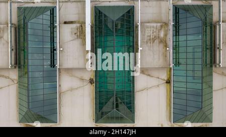 Vista ravvicinata dall'alto delle moderne finestre lucernari a forma triangolare sul tetto con una tinta verde sul tetto di un centro commerciale Foto Stock