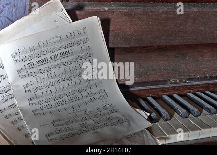 Pianoforte antico con una partitura musicale, in un soggiorno di una casa abbandonata nel Nord Italia. UrbEx in Italia Foto Stock