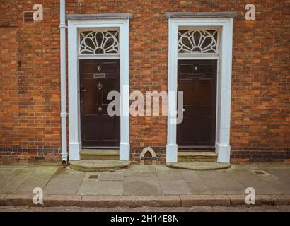 Vista sulla strada di due porte con finestre a luce di sole decorative. Al centro delle porte si trova un raschietto fisso in ferro. Foto Stock
