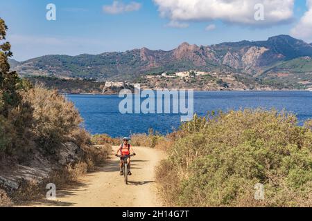 Bella donna che guida la sua mountain bike elettrica sulla costa del mediterraneo, sull'Isola d'Elba, nell'Arcipelago toscano, di fronte a Porto Foto Stock