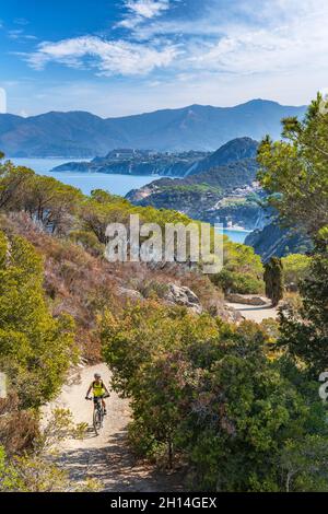 Bella donna che guida la sua mountain bike elettrica sulla costa del mediterraneo, sull'Isola d'Elba, nell'Arcipelago toscano, di fronte a Porto Foto Stock