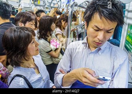 Tokyo Japan, treno della metropolitana della stazione JR Shibuya, linea Yamanote, passeggeri passeggeri pendolari, uomo asiatico cellulare cercando di leggere messaggi di testo donna Foto Stock