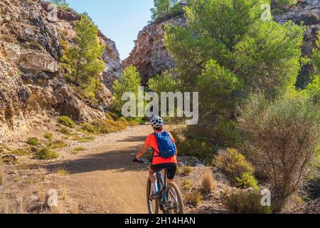 Bella donna che guida la sua mountain bike elettrica sulla costa del mediterraneo, sull'Isola d'Elba, nell'Arcipelago toscano, di fronte a Porto Foto Stock