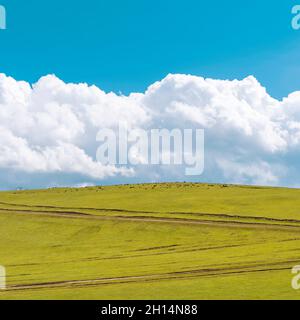 Collina verde con strade sterrate e nuvole soffici sopra di essa. Animali che pascolo sulla cima della collina. Foto Stock