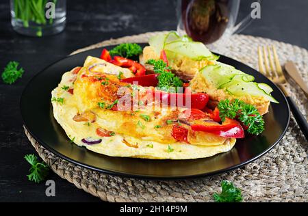 Colazione. Omelette con paprika, formaggio e pomodori con sandwich su piatto nero. Frittata - frittata italiana. Foto Stock