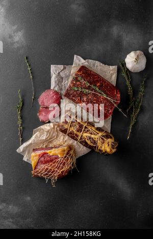 composizione ancora vita con molti pezzi di prosciutto secco affumicato rosso su un tagliere di legno, vista dall'alto Foto Stock