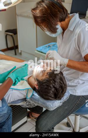 Dentista femminile di origine ispanica che controlla i denti di un giovane caucasico Foto Stock