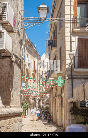 Strada stretta nel centro storico di Bari, Puglia, Italia, in una giornata estiva con bandiere italiane e coppia di turisti, verticale Foto Stock