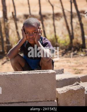 Singolo bambino africano in un villaggio in Botswana in attesa nel cortile, triste volto Foto Stock