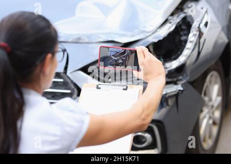 L'agente assicurativo scatta foto dei danni all'auto dopo un incidente sullo smartphone Foto Stock