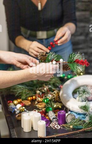 Due donne stanno preparando la corona di avvento e le decorazioni di Natale. In verticale. Foto Stock
