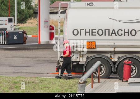 Bielorussia, Bobruisk - 02 settembre 2020: Ragazza in tute e elmetto operatore stazione di gas accanto al trasporto auto prodotti infiammabili. Foto Stock