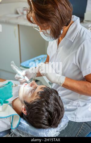 Dentista femminile di origine ispanica che controlla i denti di un giovane caucasico Foto Stock