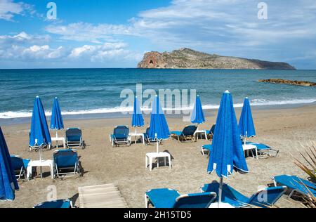 Creta isola, Grecia Agia Marina spiaggia vicino Chania ombrelloni e sedie a sdraio sulla sabbia roccioso affioramento all'orizzonte Foto Stock