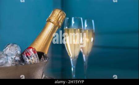 Una bottiglia di champagne all'interno di un cubo con ghiaccio con due bicchieri di champagne su sfondo blu Foto Stock