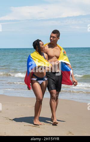 Coppia avvolta in una bandiera venezuelana mentre camminando insieme lungo la spiaggia. Foto Stock