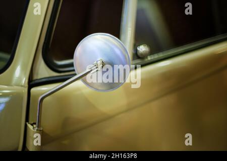 Primo piano di uno specchio arrotondato di una classica auto di colore giallo. Foto Stock