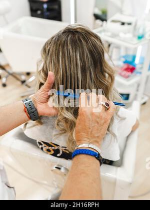 Alto angolo di raccolto anonimo parrucchiere pettinare i capelli di irriconoscibile cliente femminile in parrucchiere Foto Stock