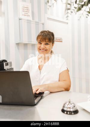 Vista laterale del giovane maschio asiatico con smartphone in mano Inserimento della carta nel terminale ATM per il prelievo di contanti in città via Foto Stock