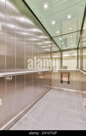 Interno di una lunga cabina con pannelli e ringhiere in metallo con riflessi di lampade luminose sul soffitto in un edificio contemporaneo Foto Stock