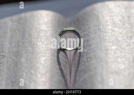 Un anello d'argento tra le pagine di un libro che forma una forma di cuore con la sua ombra al sole Foto Stock