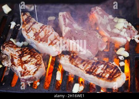 Barbecue Grill Pit con incandescente e fiammeggiante caldo, bistecche crude e cipolla, cibo di fondo, primo piano. Messa a fuoco selettiva. Foto Stock