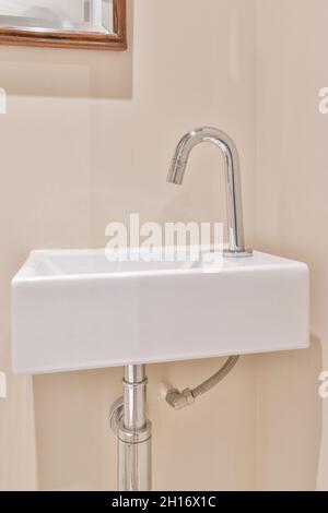 Lavello in ceramica bianca con rubinetto cromato lucido installato su parete beige in bagno Foto Stock