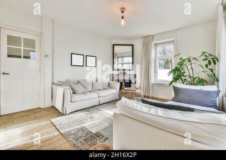 Interno contemporaneo del soggiorno con tappeto tra divani con cuscini e plaid in casa luminosa Foto Stock