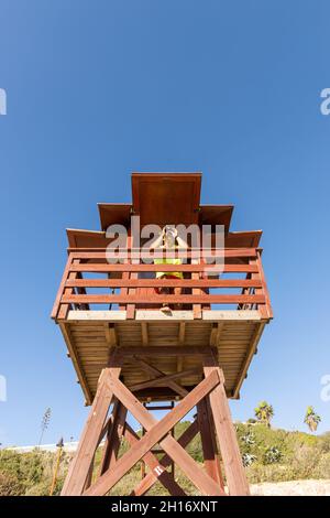 Basso angolo di visione attraverso binocoli su torre di avvistamento in legno, mentre supervisiona la sicurezza in mare contro il cielo blu senza nuvole Foto Stock