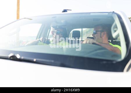 Vista laterale del bagnino negli occhiali da sole che guidano l'auto vicino al maschio parlando sul ricetrasmettitore radio durante la giornata di lavoro Foto Stock