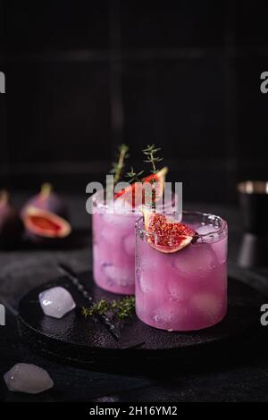 Cocktail di fichi viola con ghiaccio e timo su sfondo scuro Foto Stock