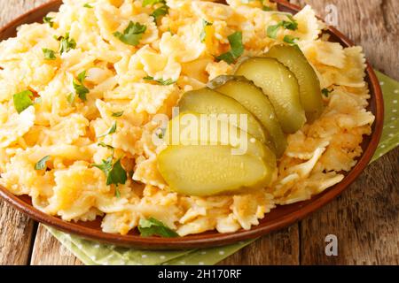 Piatti europei Pasta con patate e cipolle servita con sottaceti primo piano in un piatto sul tavolo. Orizzontale Foto Stock