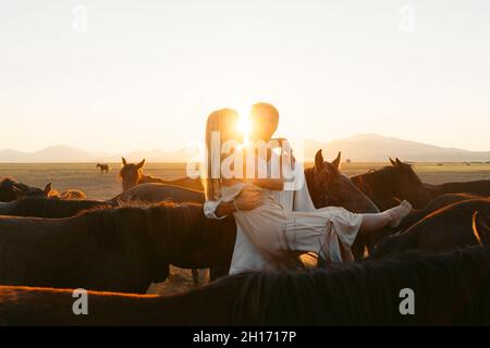 uomo che tiene la ragazza leata fiera tra i cavalli in pascolo di campagna mentre si guarda l'un l'altro Foto Stock