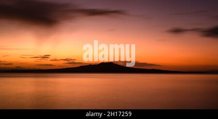 Spiaggia di Milford all'alba con nubi di pioggia che si aggirano sull'isola di Rangitoto, Auckland. Foto Stock