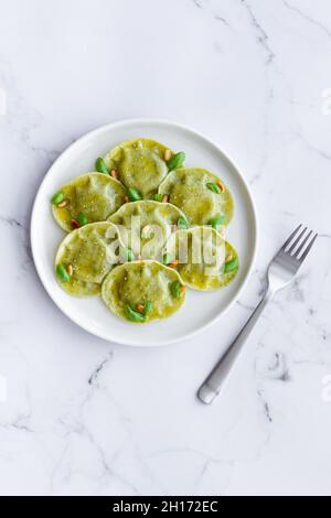 Vista dall'alto di gustosi ravioli con basilico decorato con pinoli serviti su piatto rotondo bianco su tavolo in cucina luminosa Foto Stock