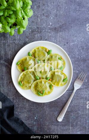 Vista dall'alto di gustosi ravioli con basilico decorato con pinoli serviti su piatto rotondo bianco su tavolo in cucina luminosa Foto Stock