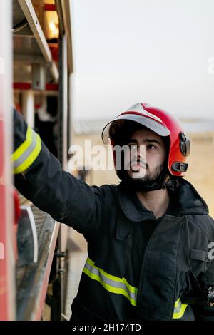 Operatore tranquillo che indossa una uniforme protettiva e un elmetto rosso che funziona all'interno di un camion antincendio Foto Stock