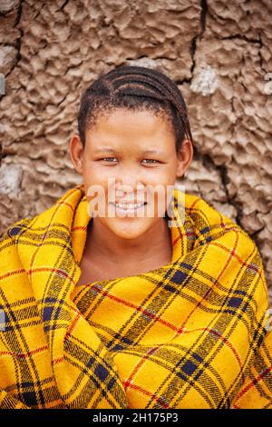 Una giovane ragazza bushman da Central Kalahari, villaggio New Xade in Botswana, di fronte a una coperta il suo shack Foto Stock