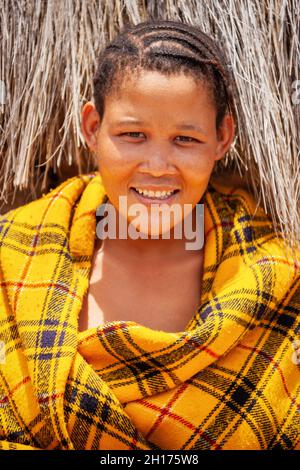 Una giovane ragazza bushman da Central Kalahari, villaggio New Xade in Botswana, di fronte a una coperta il suo shack Foto Stock